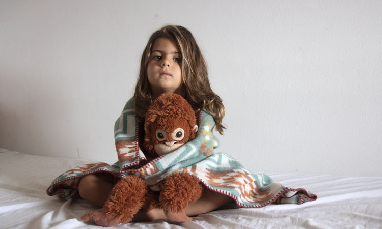 Girl with cuddly toy and blanket on a bed