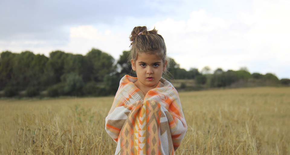 Girl in a field covering herself with a baby blanket